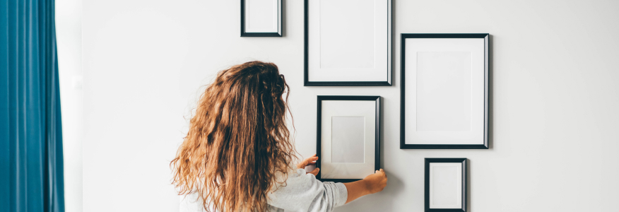 A woman hanging a frame on a wall.